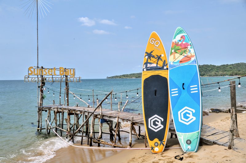 Colorful paddleboards on beach with pier and green hills
