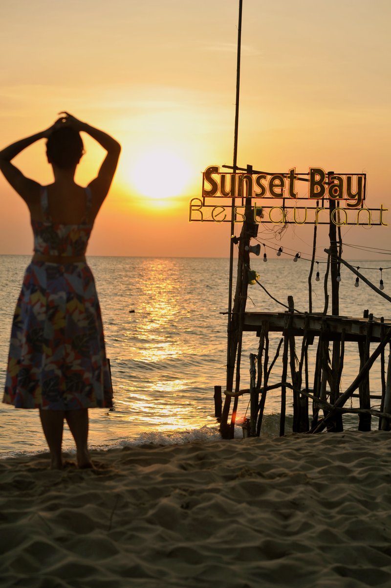 Woman in floral dress gazing at sunset on the beach